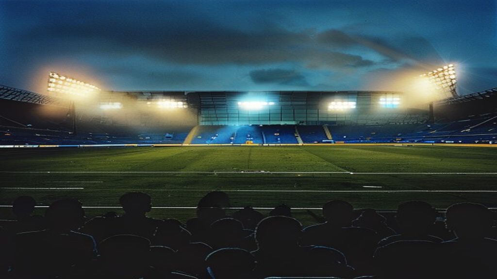 Empty stadium floodlights at dusk with crowd silhouettes and team colours in the stands