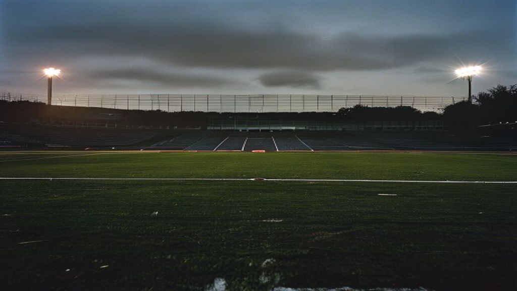 Empty football stadium at dusk with fading floodlights